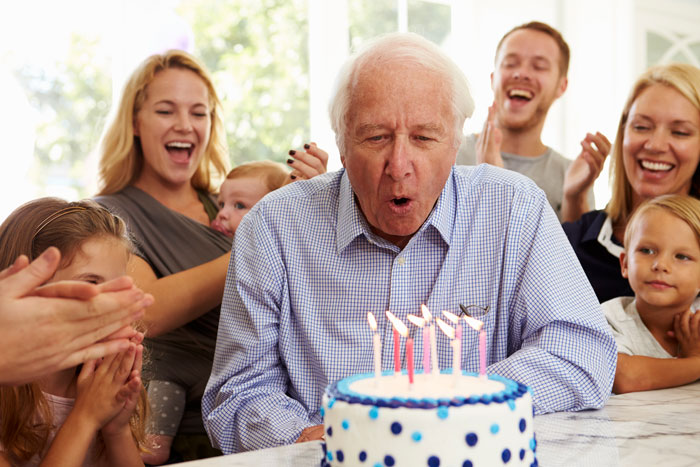 grandfather blowing out birthday cake candles at a birthday party with family