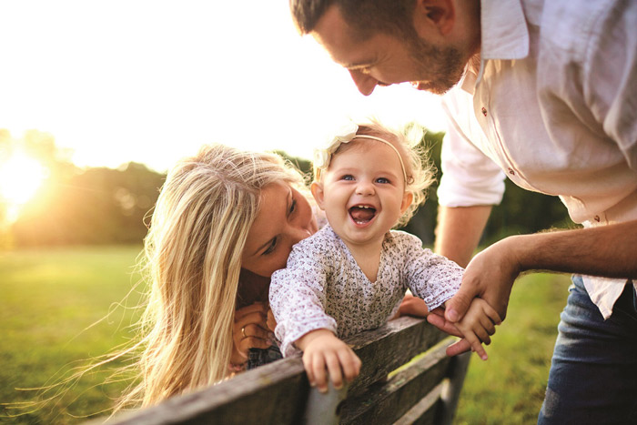young smiling couple with toddler on a park bench smiling